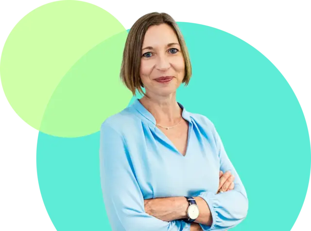 Tanja Faßbinder, eine Frau mit kurzen hellbraunen Haaren und hellblauer Bluse, steht mit verschränkten Armen und lächelt vor einem türkisfarbenen und hellgrünen abstrakten Hintergrund.