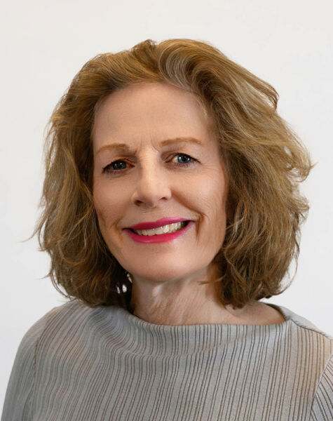 Eine lächelnde Frau, Laura Burckhardt, mit hellbraunem, schulterlangem Haar, trägt ein graues, strukturiertes Oberteil und posiert vor einem schlichten weißen Hintergrund.