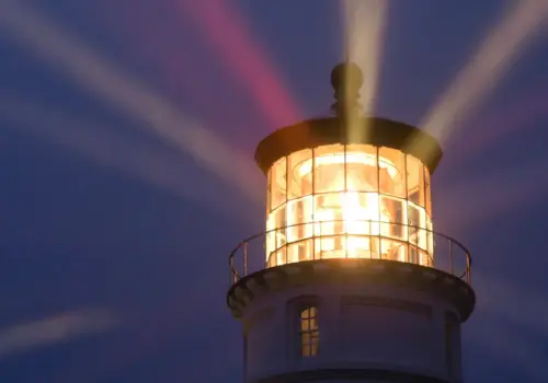 Ein Leuchtturm bei Nacht, dessen helles Licht in den dunklen Himmel strahlt und durch die Beleuchtung der Umgebung Führung in unsicheren Zeiten symbolisiert.