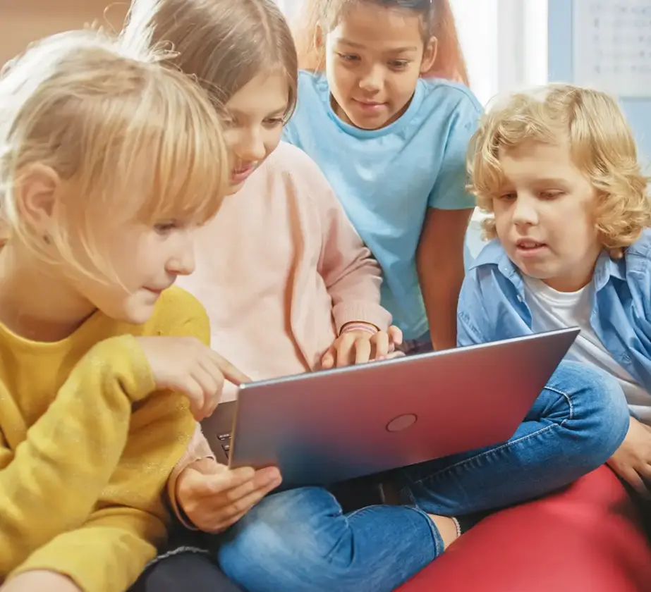 Vier kleine Kinder sitzen dicht beieinander, lächeln und schauen auf einen Laptop-Bildschirm. Sie denken darüber nach, wie frühe Neugier dazu beitragen kann, die Lernkultur in Unternehmen zu verbessern, indem sie Engagement und Teamarbeit fördert.