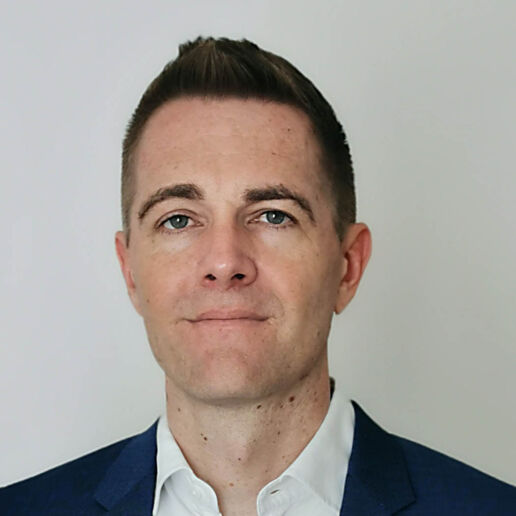 Benjamin Stahl, ein Mann mit kurzen braunen Haaren, trägt ein marineblaues Jackett und ein weißes Hemd. Er steht vor einem schlichten hellen Hintergrund und blickt mit neutralem Gesichtsausdruck direkt in die Kamera.