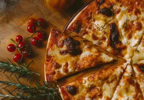 Eine in Scheiben geschnittene Käsepizza auf einer Holzoberfläche, garniert mit Rosmarinzweigen und einer Gruppe Kirschtomaten in der Nähe.
