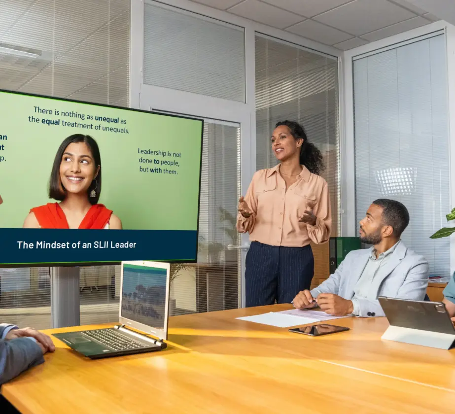 Four colleagues sit around a conference table as a woman presents slides on The Mindset of an SJI Leader, discussing equal treatment, leadership, and recognizing learning needs in companies.