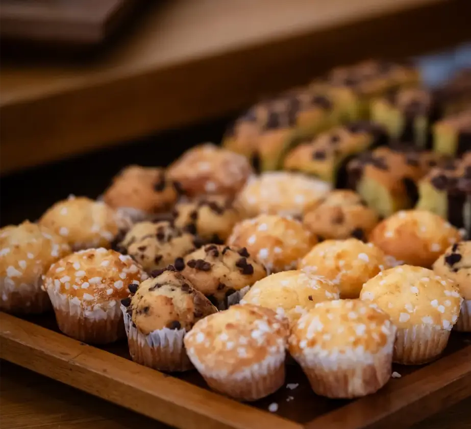 Ein Holztablett, gefüllt mit verschiedenen Mini-Muffins, darunter Schokoladen- und Zuckermuffins, steht fein säuberlich aufgereiht auf einem Holztisch - perfekt, um erfolgreiche Trainings- und Coachingprojekte zu feiern.