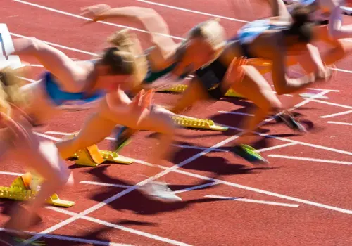 Mehrere Athleten in Bewegungsunschärfe sprinten auf einer roten Bahn aus den Startblöcken, aufgenommen zu Beginn eines Rennens - ähnlich wie Teams, die sich auf Lernsprints begeben und dynamische Bewegung und Energie demonstrieren.