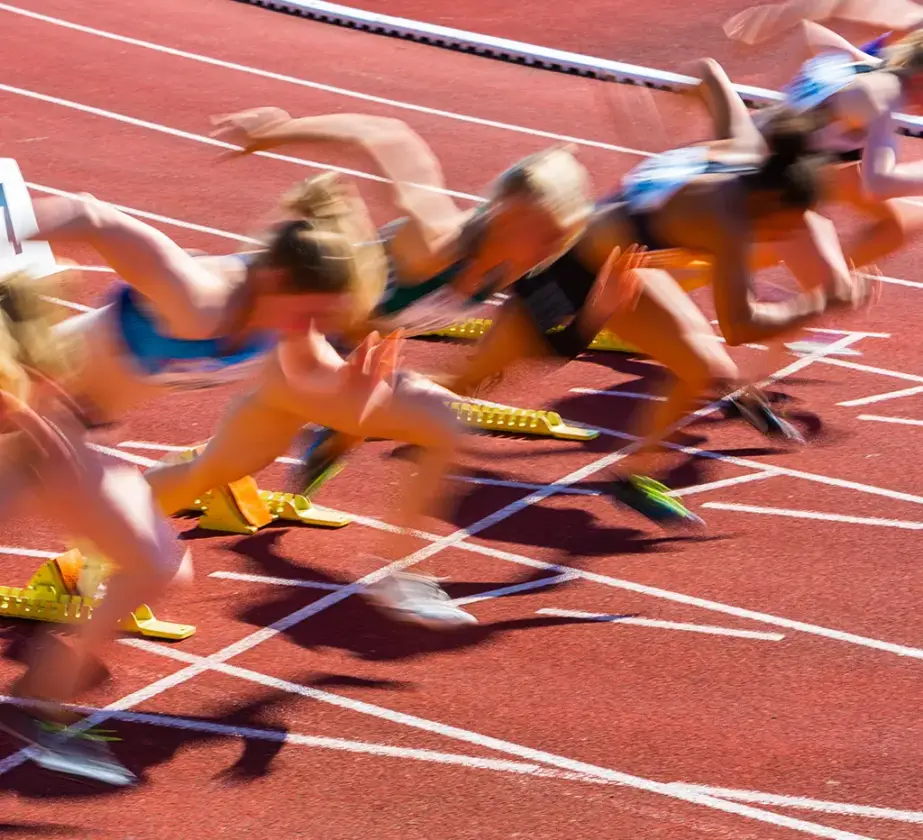 Mehrere Athleten in Bewegungsunschärfe sprinten auf einer roten Bahn aus den Startblöcken, aufgenommen zu Beginn eines Rennens - ähnlich wie Teams, die sich auf Lernsprints begeben und dynamische Bewegung und Energie demonstrieren.