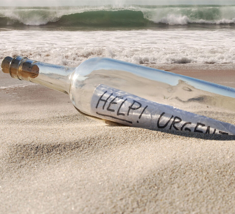 Eine Glasflasche mit einem aufgerollten Zettel mit der Aufschrift "HELP! URGENT" liegt auf dem Sandstrand in der Nähe des Ufers und symbolisiert die Notwendigkeit, Lernbarrieren in der Personalentwicklung abzubauen, während im Hintergrund die Wellen sanft rollen.