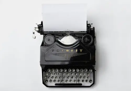 A vintage black typewriter with a blank sheet of paper inserted, photographed from above on a plain white background—an ideal image for illustrating the process of recognizing learning needs in companies.
